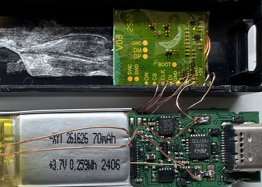 Placa verde del implante con cables de cobre soldados a la placa base de un Ledger Nano X, junto a la batería