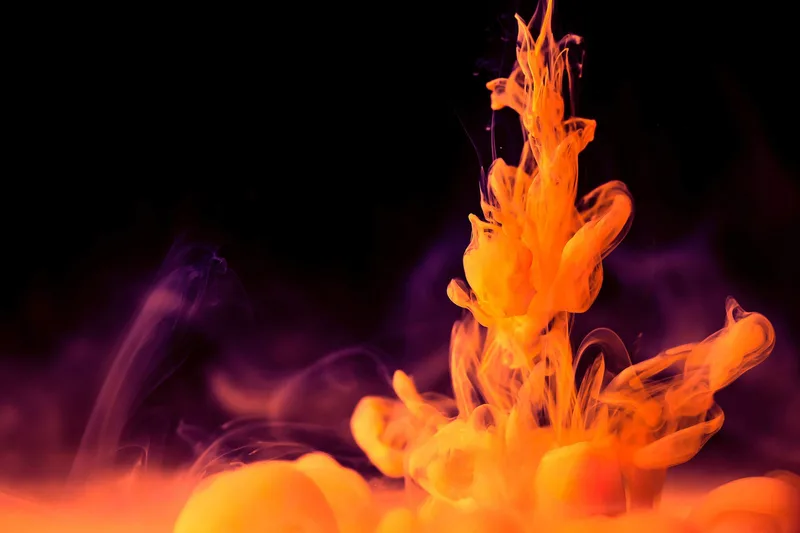 Humo de tinta naranja y morada ascendiendo sobre fondo negro