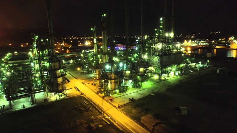 Vista aérea nocturna de una refinería industrial iluminada con tuberías y torres